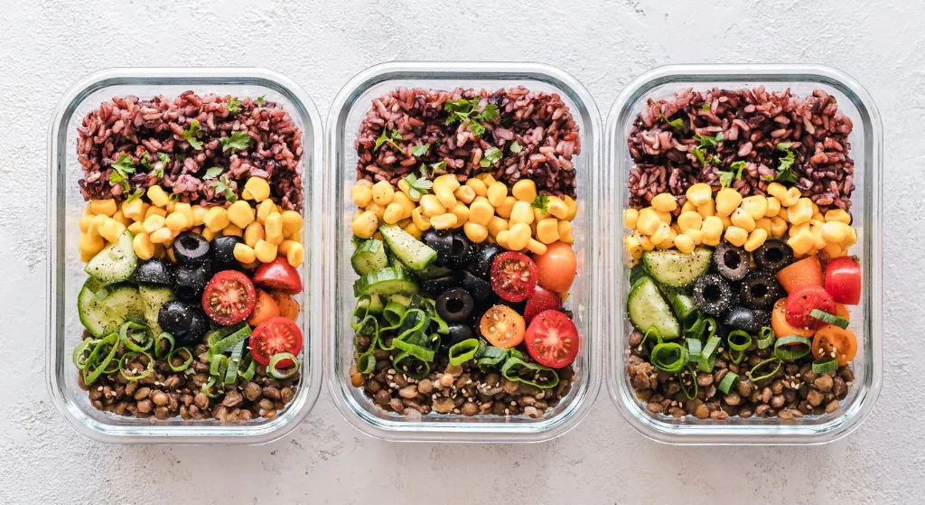 Colorful healthy meal prep with corn, olives, tomatoes, and lentils in glass containers. Perfect for mindful eating